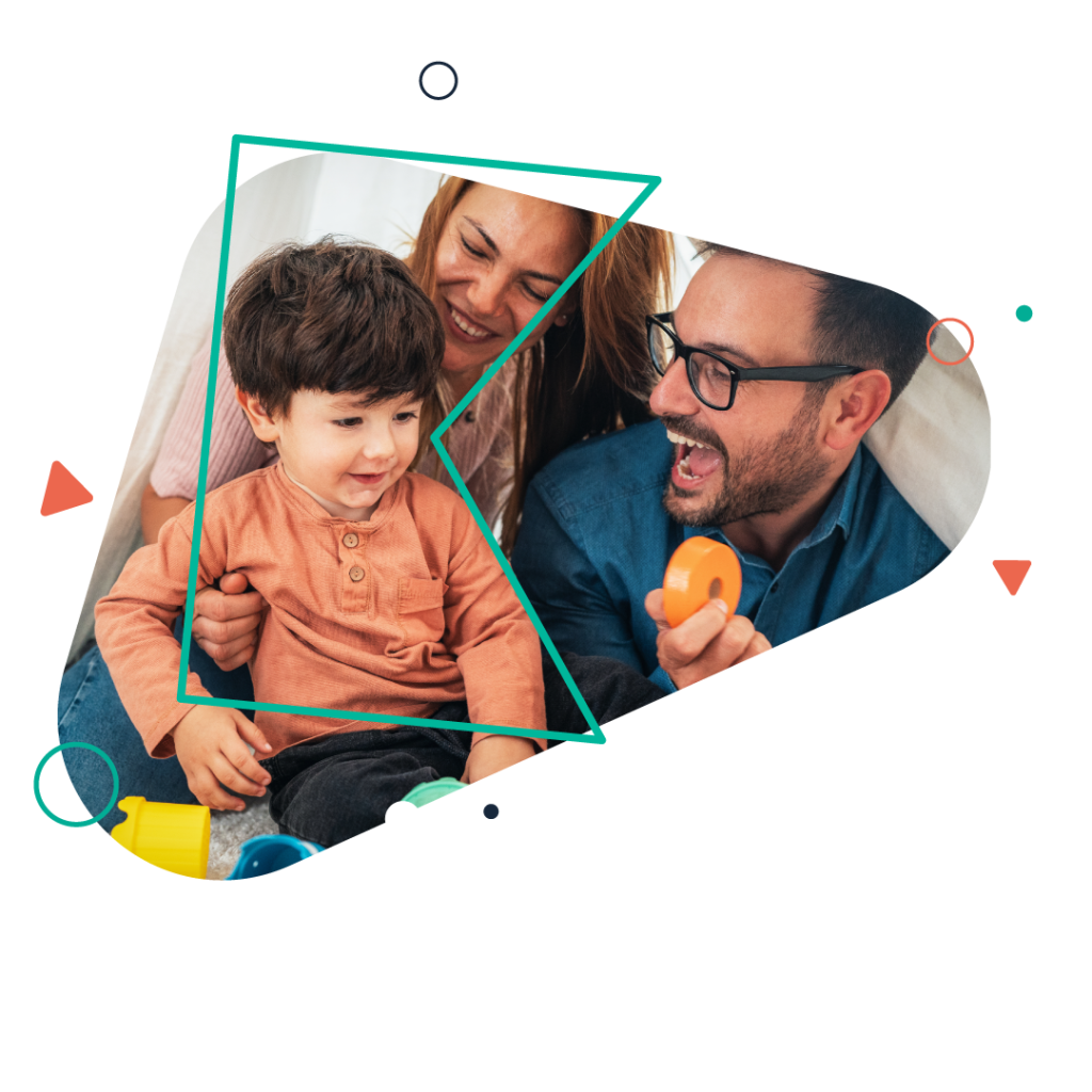 A man with facial hair and glasses and a woman with red hair hold a smiling toddler while playing with colourful toys