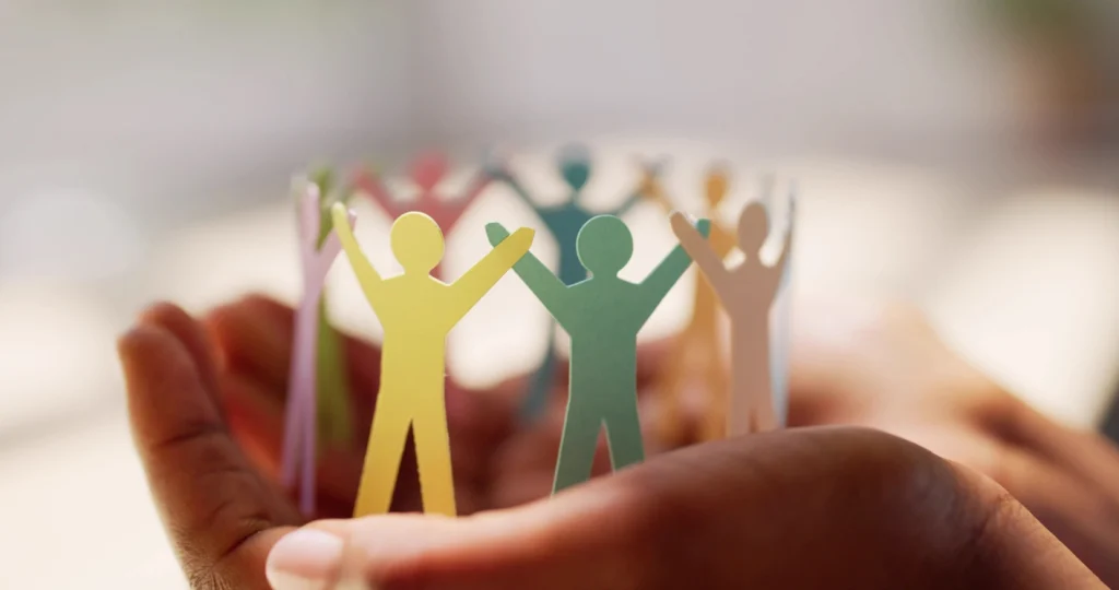 Hands holding a circular paper sculpture of colourful figures holding hands
