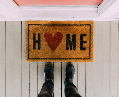 downwards view of feet standing in front of a doormat that says 