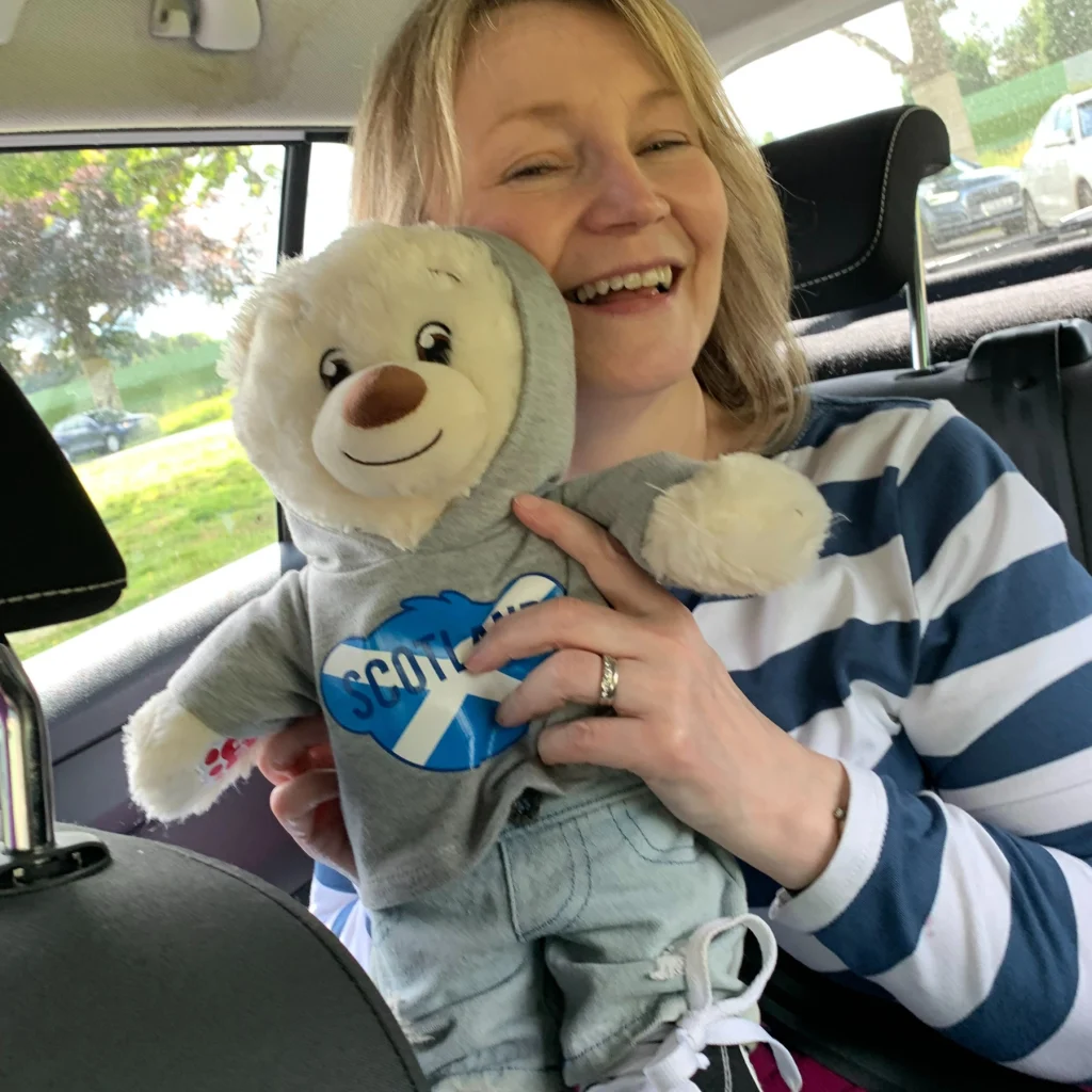 female foster carer smiling in a car enjoying a teddy bear in Stirling