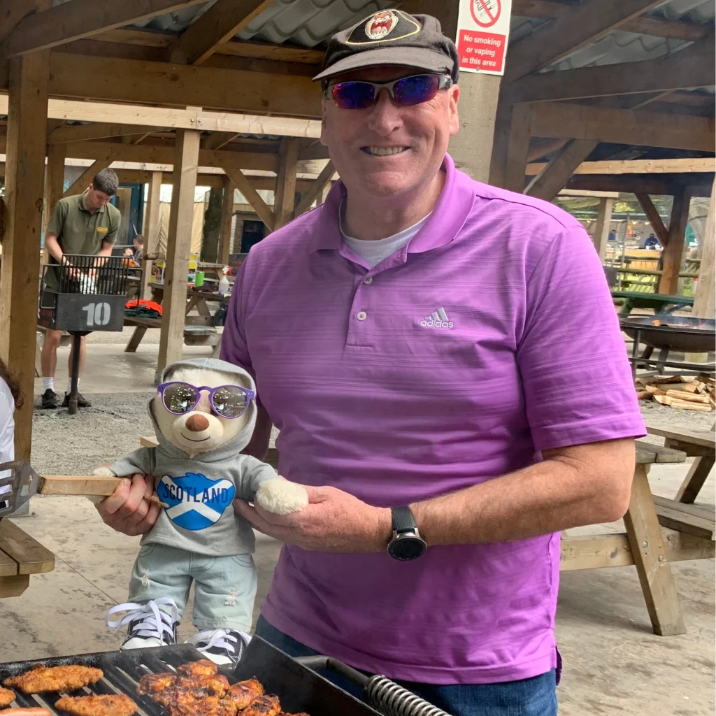 male foster carer smiling and holding a teddy bear at Stirling park