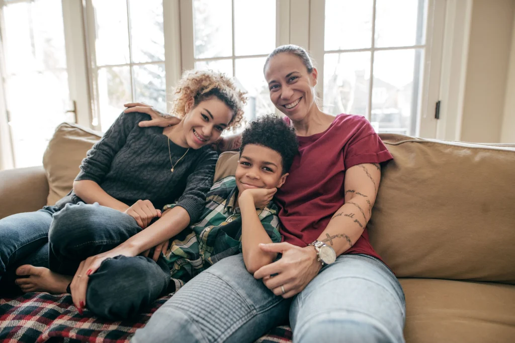 two female foster parents smiling with young boy on their sofa
