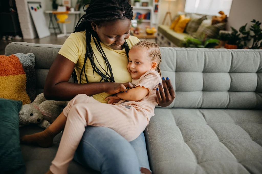 female foster parent hugging a little girl on a couch