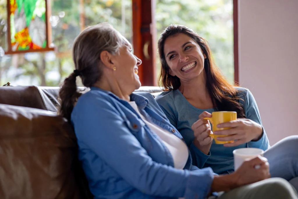 two women on a couch enjoying coffee and smiling