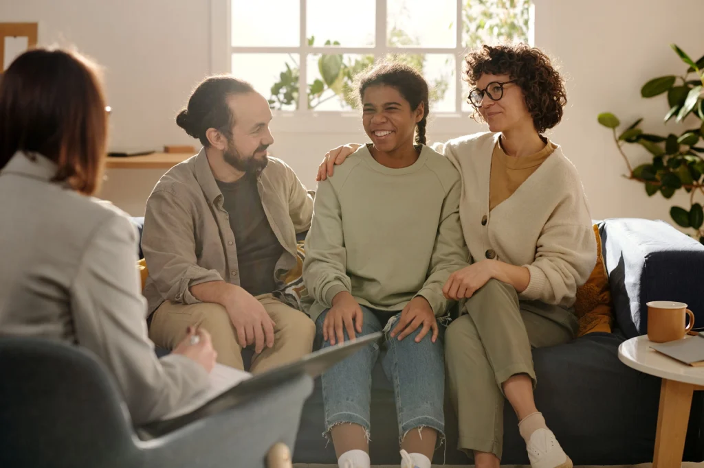 teenager and foster parents laughing with a social worker in their home
